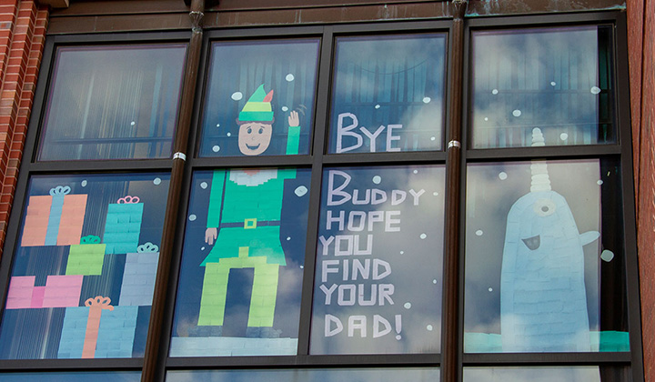 Res hall windows decorated in sticky notes to display Buddy the Elf and a narwal